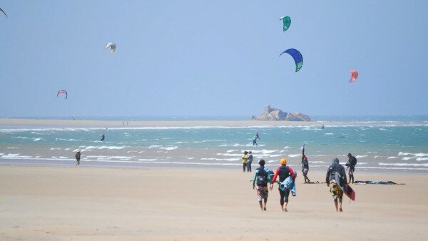Kitesurfers on Essaouira beach with colorful kites against blue sky